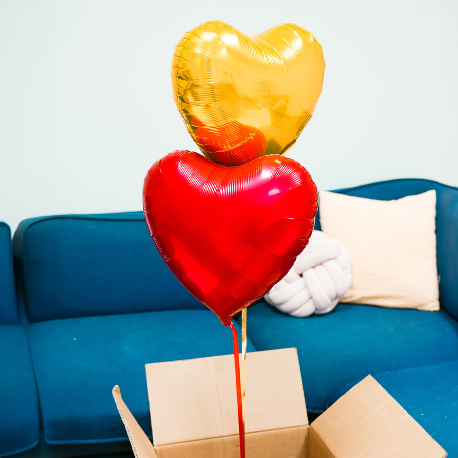 Box contenant deux ballons en forme de cœur rouge et or.