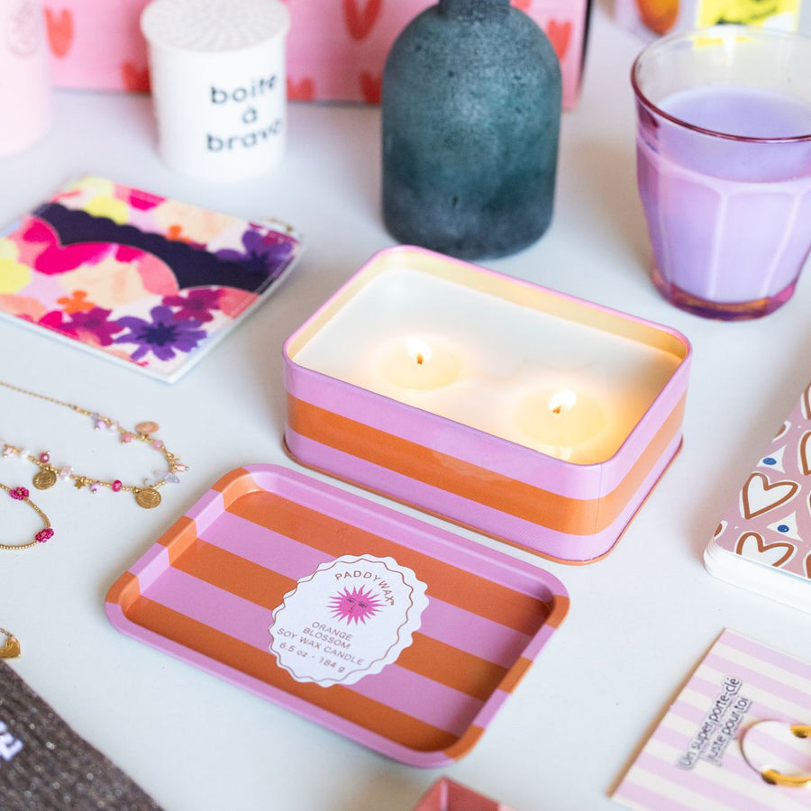 Bougie à 2 mèches avec rayures orange et rose, motif soleil.