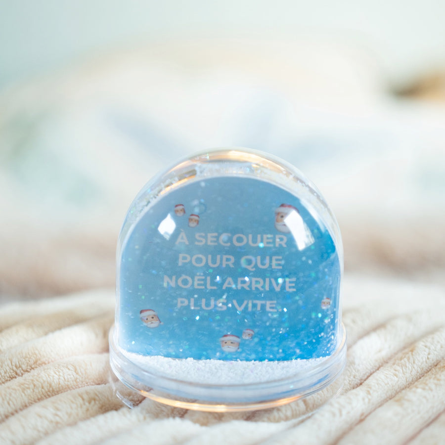 Boule à neige avec flocons scintillants et décor festif.