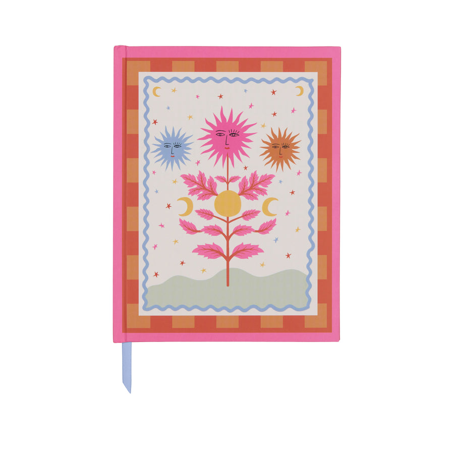 Carnet avec motif soleil sur fond hot pink, ouvert sur une table