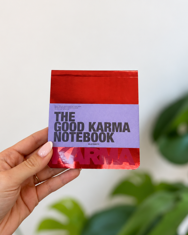 Bloc-notes Good Karma rouge et violet, tenu en main, avec lettrage noir