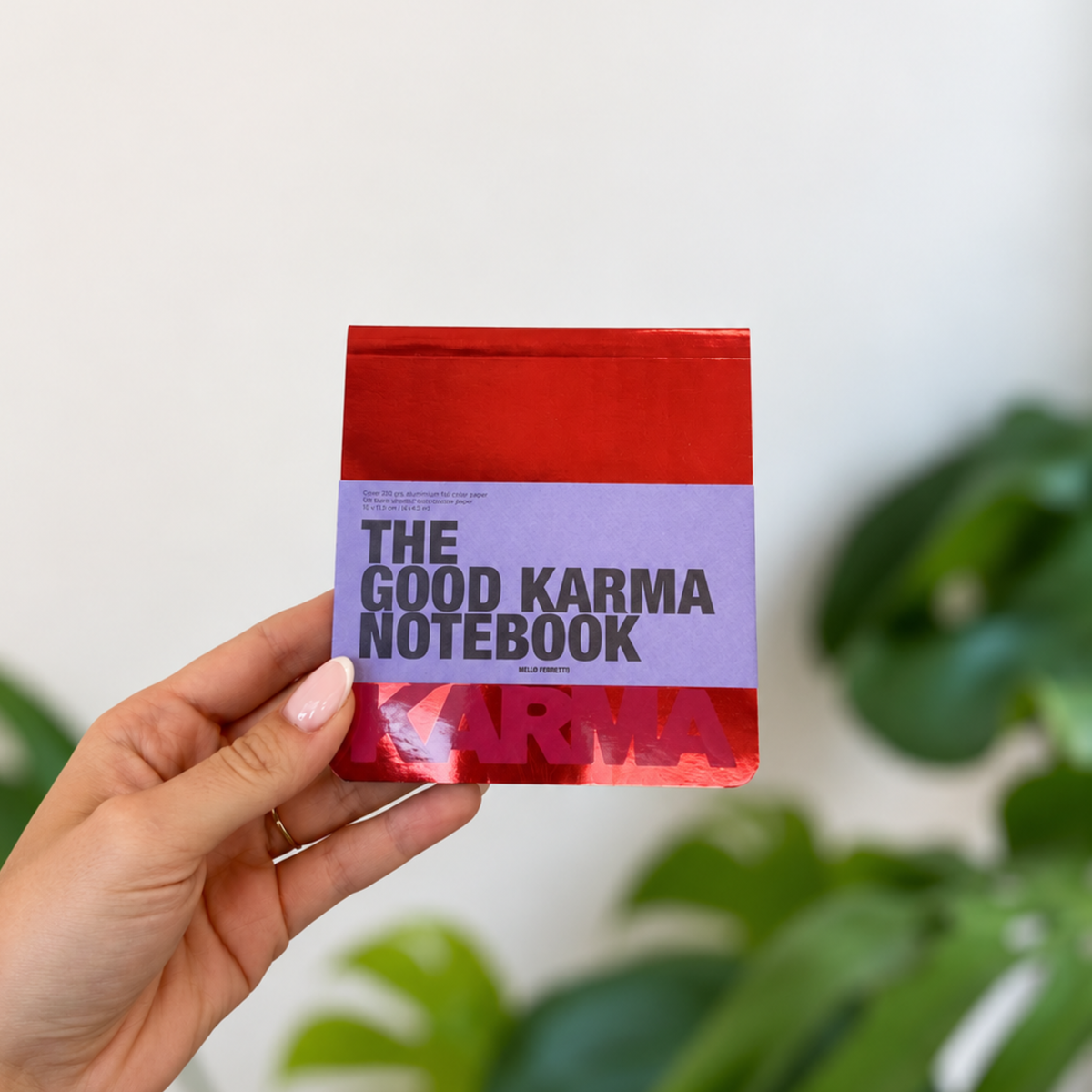 Bloc-notes Good Karma rouge et violet, tenu en main, avec lettrage noir