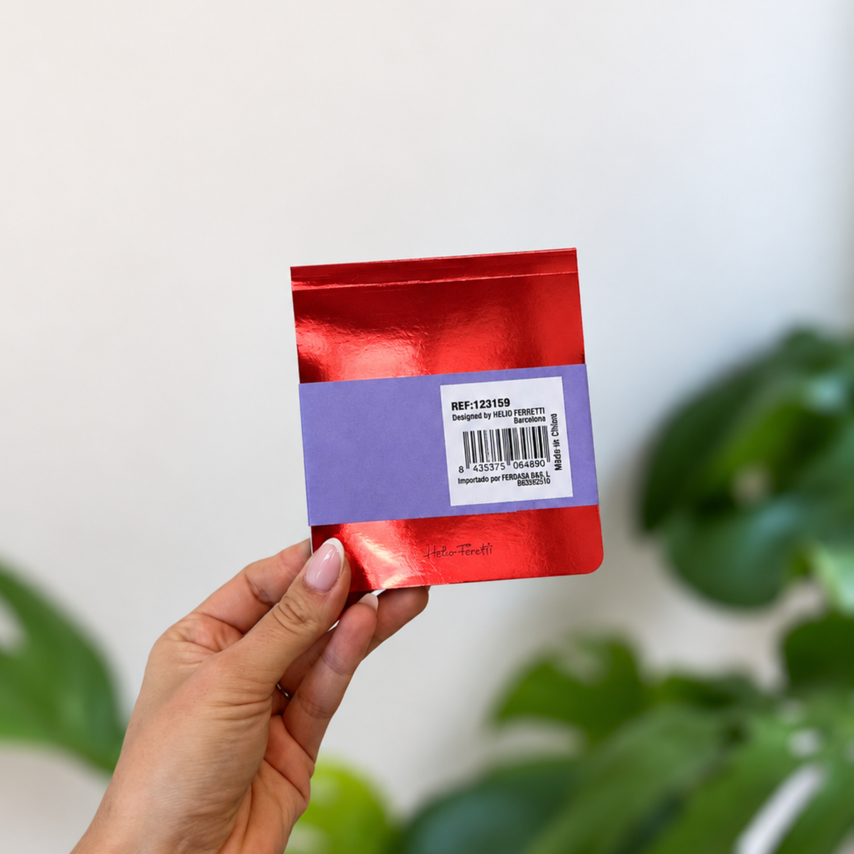 Bloc-notes rouge métallisé tenu en main, avec bandeau violet au dos