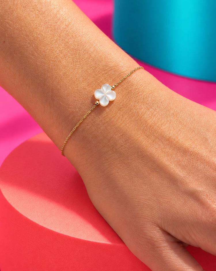 Bracelet doré à trèfle nacré bombé, porté en gros plan au poignet