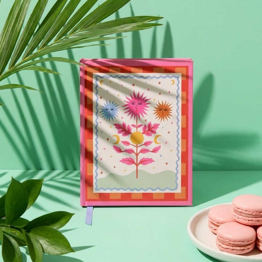 Carnet avec motif soleil sur fond hot pink, ouvert sur une table