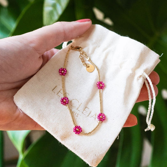 Bracelet avec marguerites roses et détails dorés en gros plan.