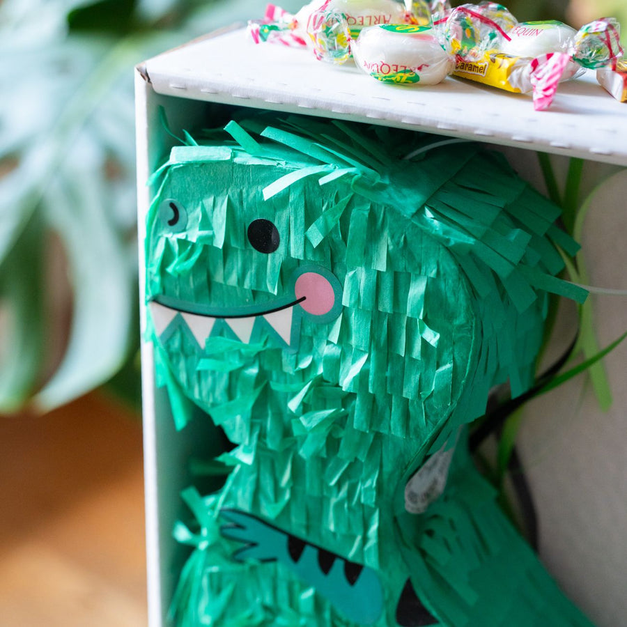 Piñata dinosaure colorée avec bonbons visibles à l'intérieur.